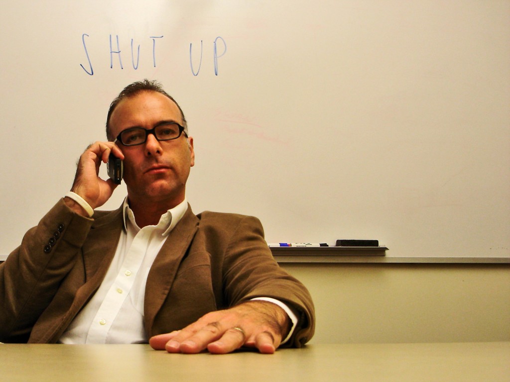 Man on phone with 'shut up' on whiteboard behind him