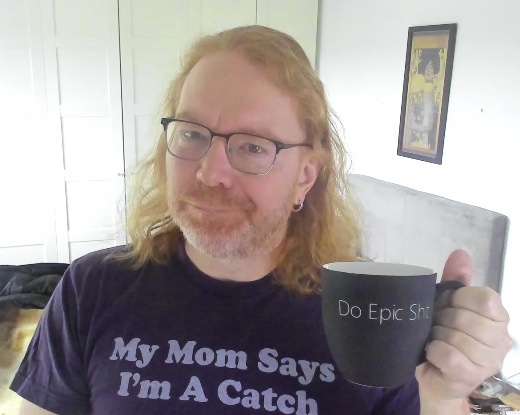 Chris Heilmann wearing a T-Shirt saying "My mom says I'm a catch" and holding a coffee cup stating "do epic shit"